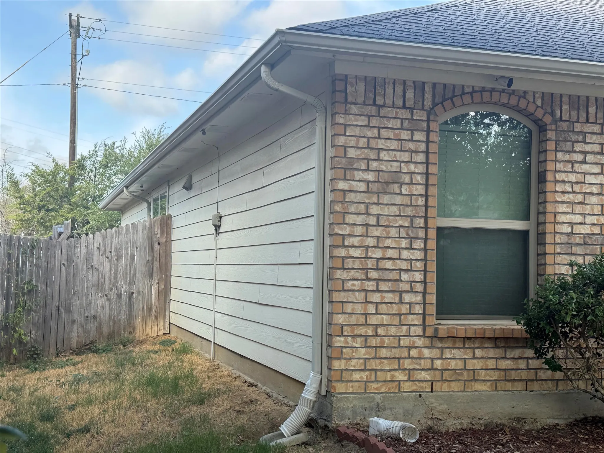 Brick exterior with arched window detail, horizontal siding, asphalt shingle roof, and white rain gutters