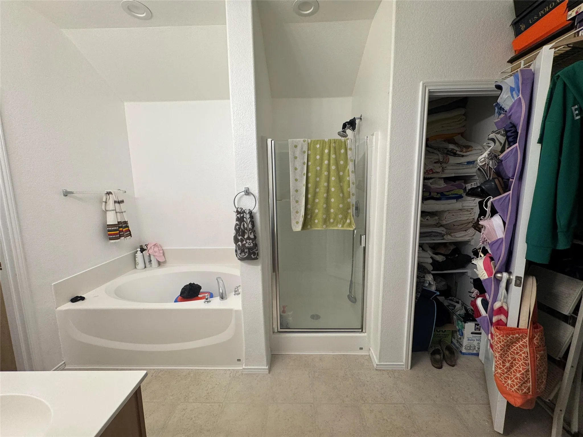 Built-in corner bathtub, glass-enclosed shower, recessed ceiling lighting, and tile flooring