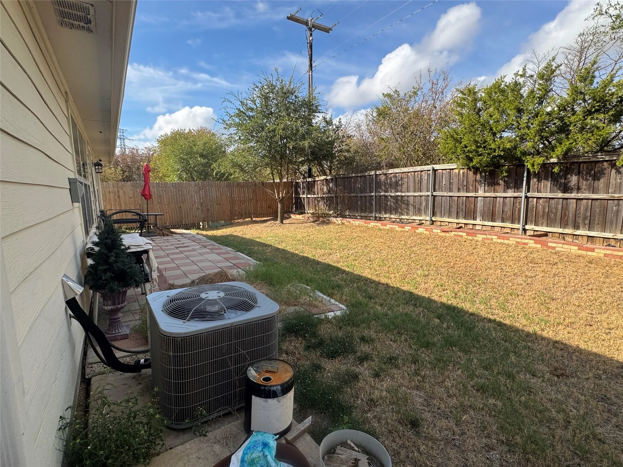 Expansive backyard featuring a wood fence, brick-lined landscaping, and a rectangular paver patio