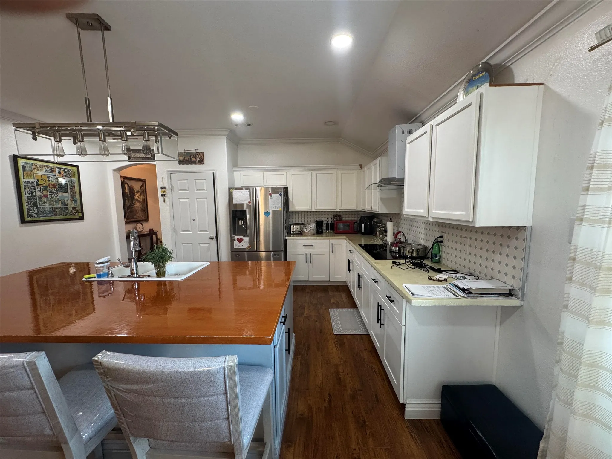 Kitchen featuring wood-finish flooring, white cabinetry, a built-in kitchen island with an integrated sink, and an overhead pendant light fixture