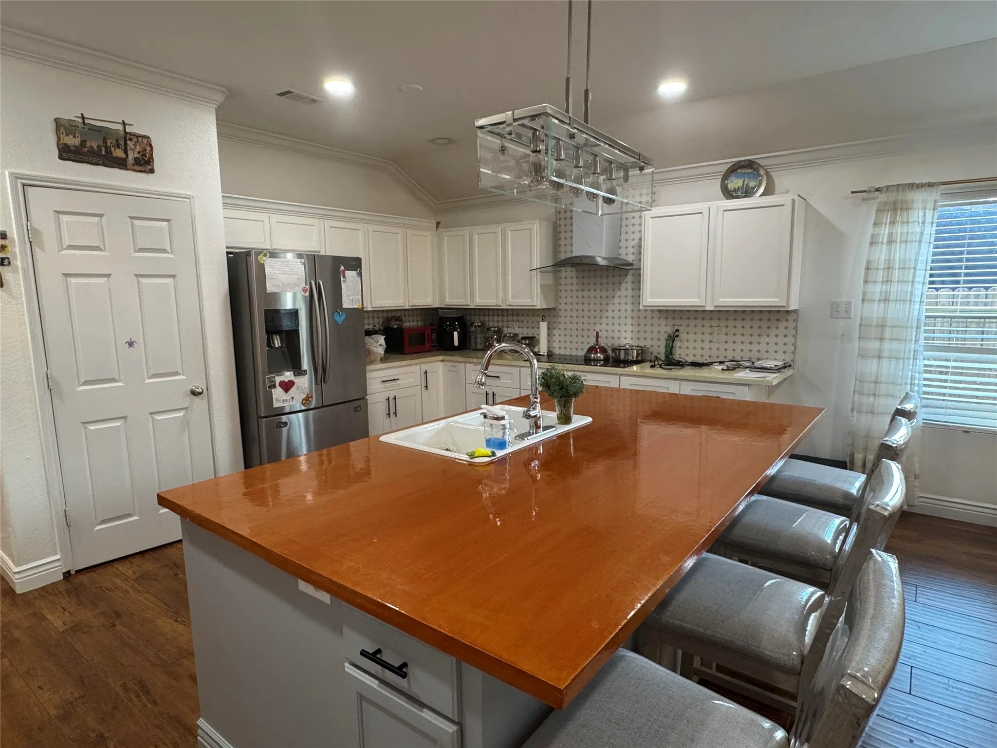 Kitchen featuring a large central island with an integrated sink, white cabinetry, a stainless steel range hood, and wood-finish flooring