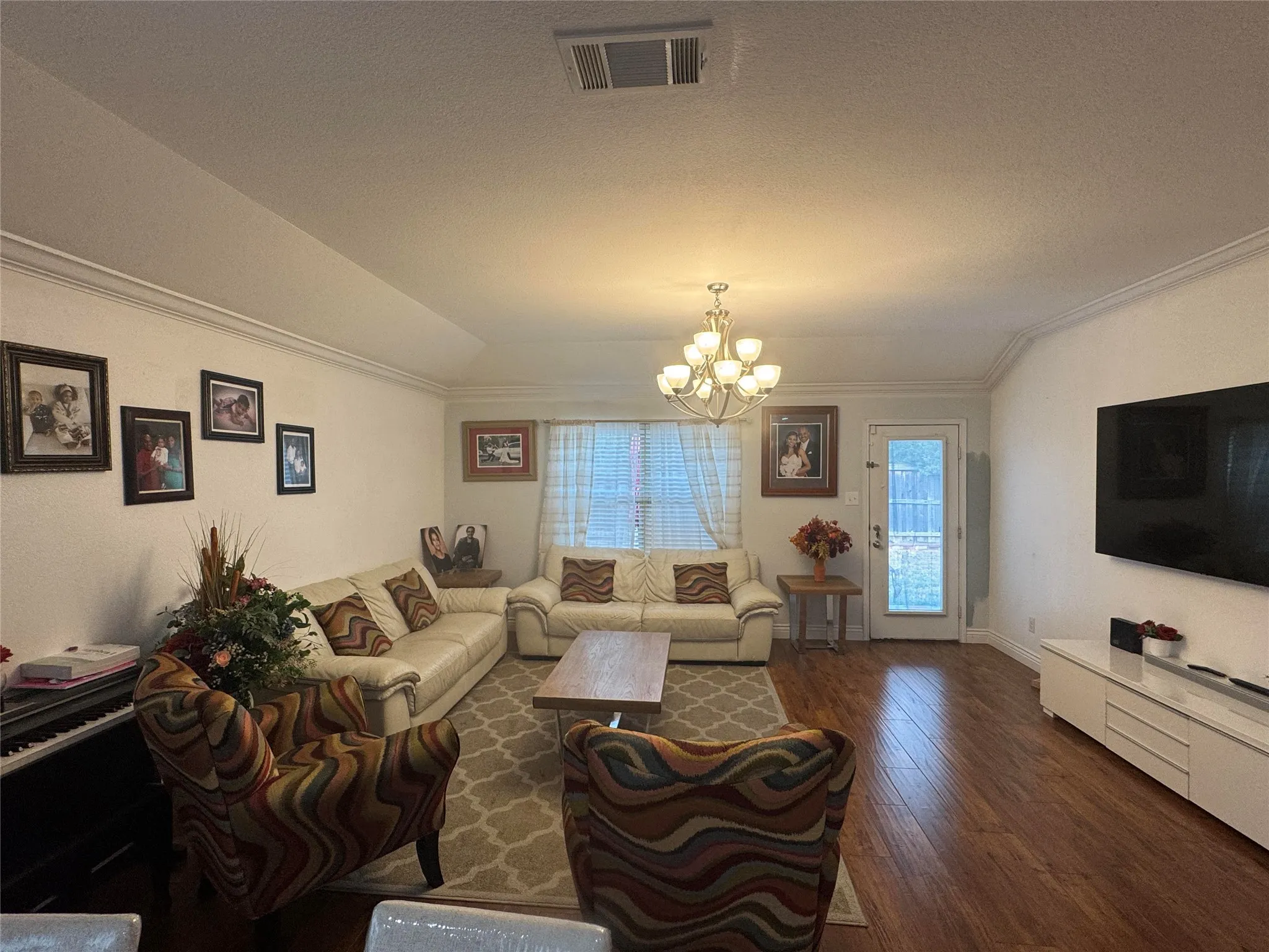 Spacious living area featuring wood-finish flooring, vaulted ceilings with crown molding, and a central chandelier