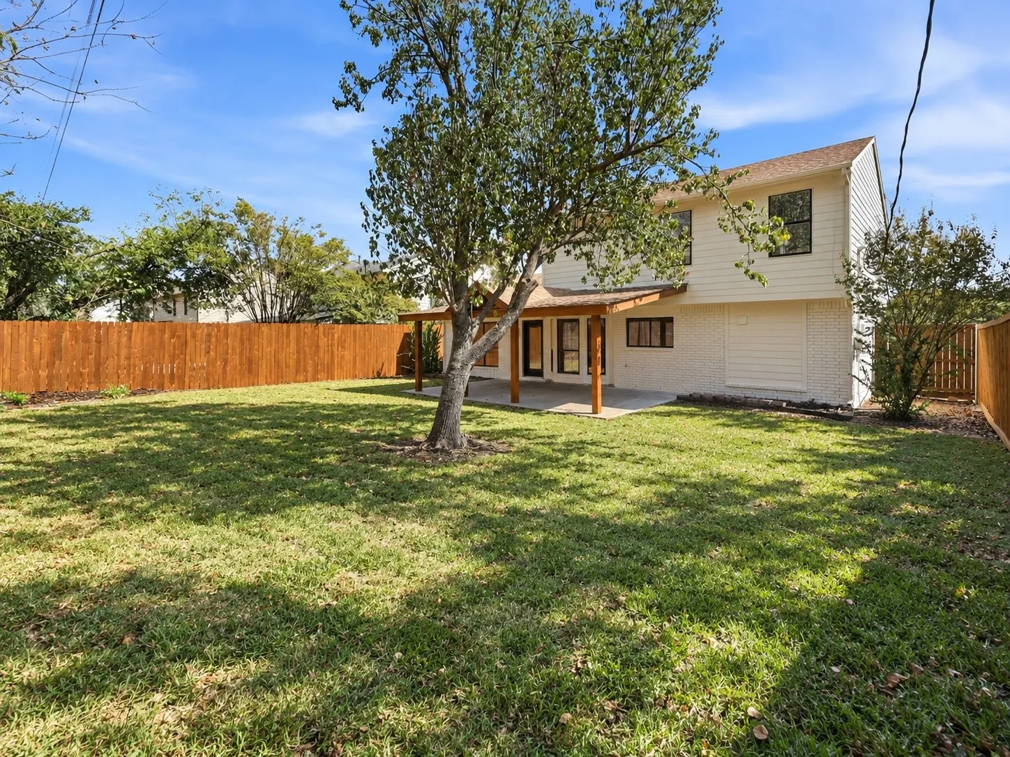 Expansive backyard featuring a manicured lawn, full privacy fencing, mature trees, and a covered patio with direct access to the interior
