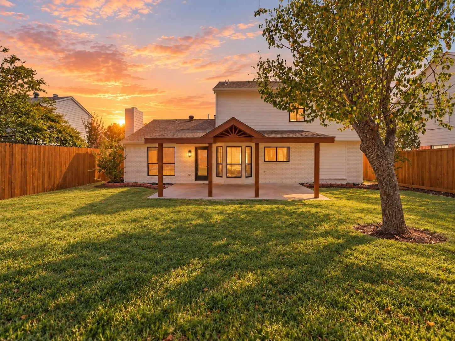 Expansive green lawn with a mature tree, a covered patio, and a wood privacy fence