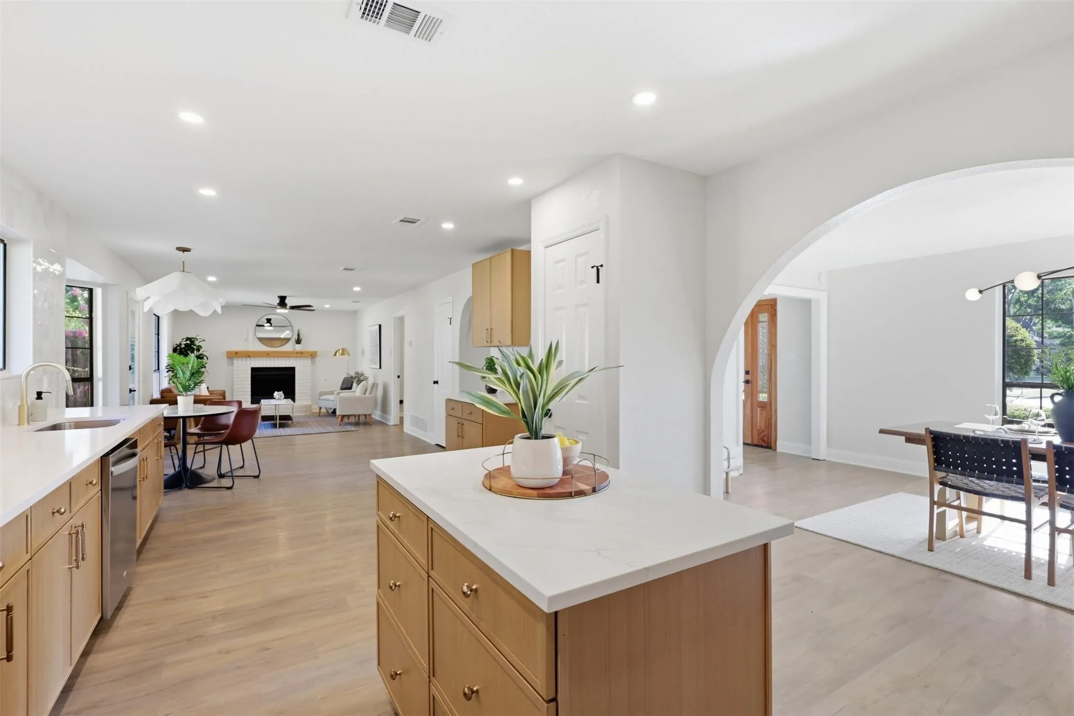 Open concept floor plan featuring a kitchen island with stone countertops, stainless steel appliances, wood-finish flooring, recessed lighting, and a fireplace with a wood mantle