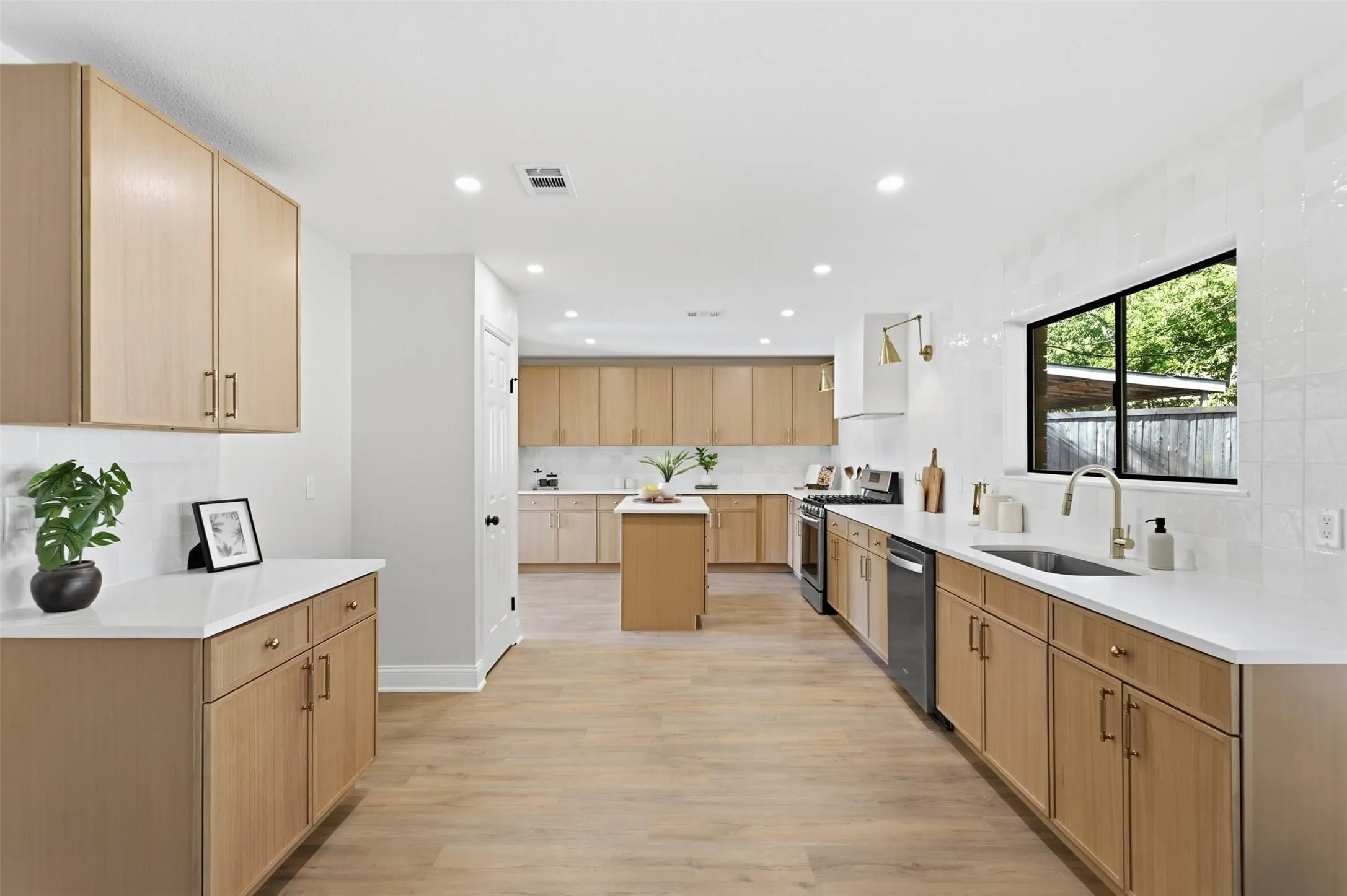 Modern kitchen with light wood-finish cabinetry, white countertops, and a full suite of stainless steel appliances