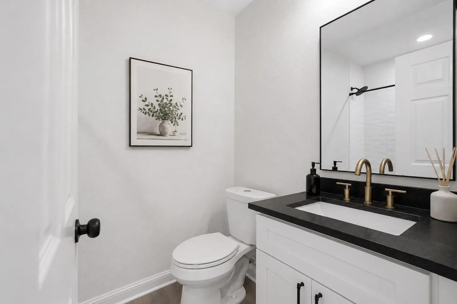 White vanity with black countertop, undermount sink, and brass-tone hardware