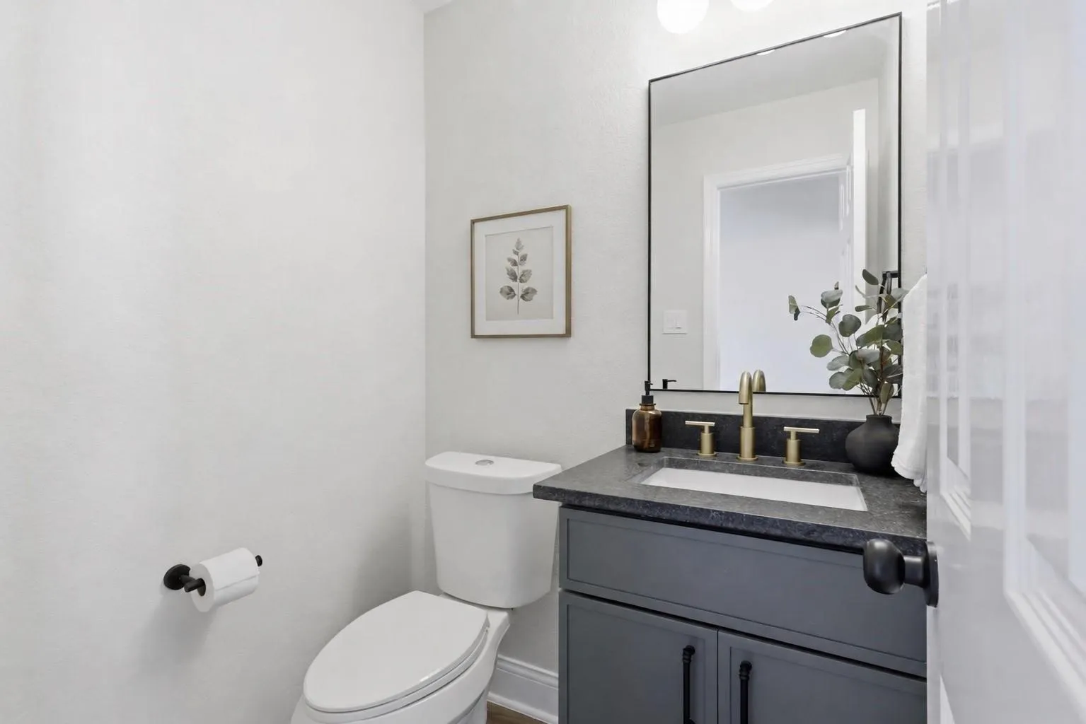 Vanity with dark countertop, undermount sink, and brass-finish faucet