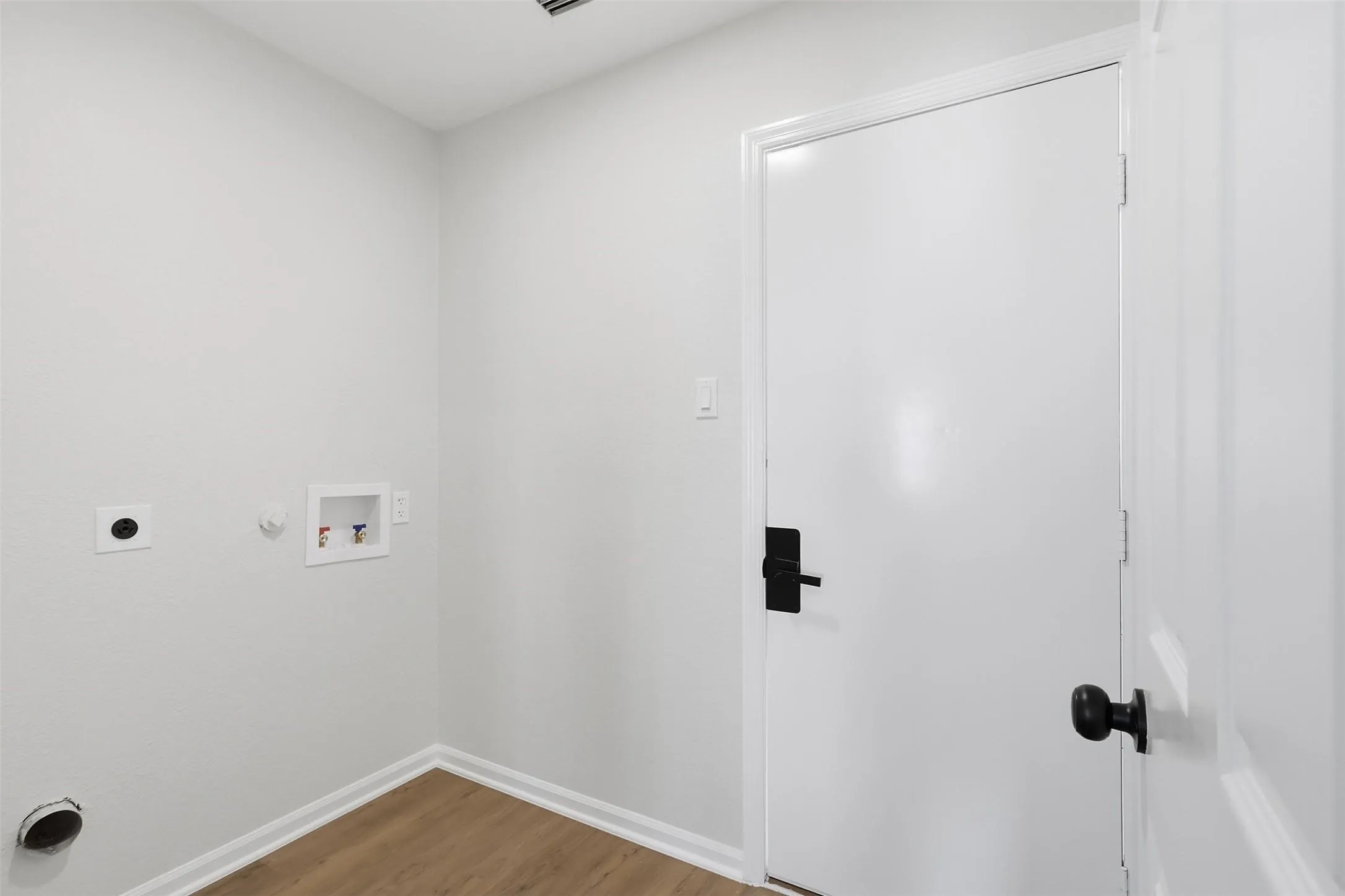 Laundry area with wood-finish flooring, white walls, and a white door with black hardware