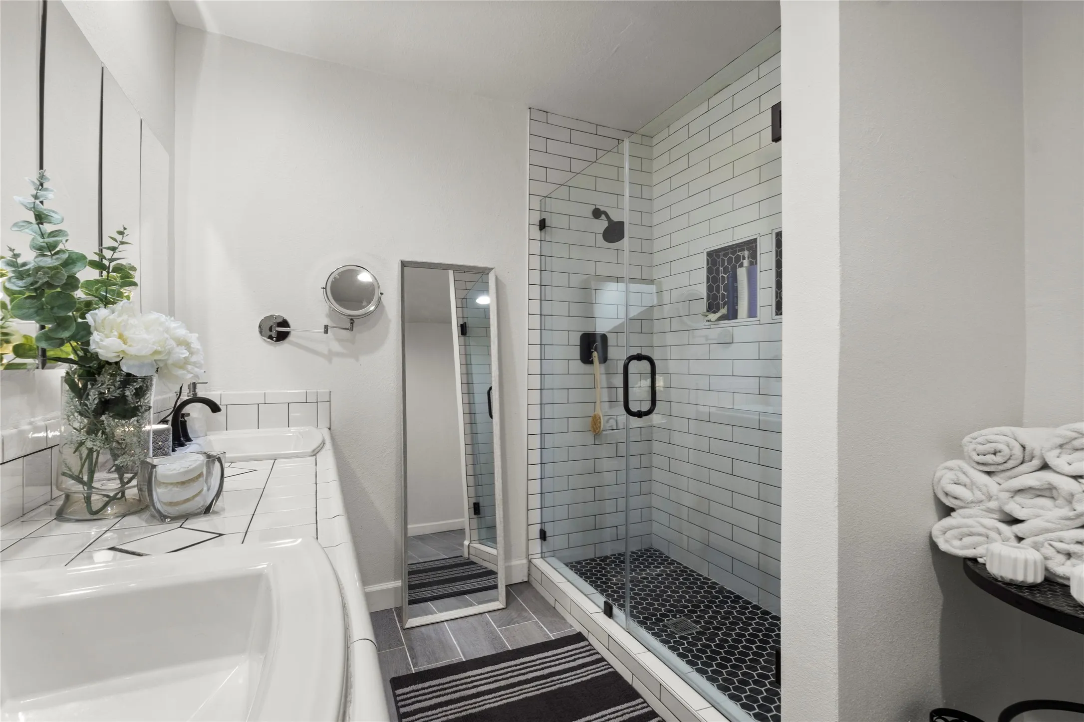 Glass-enclosed shower with subway tile surround and dark hex tile flooring