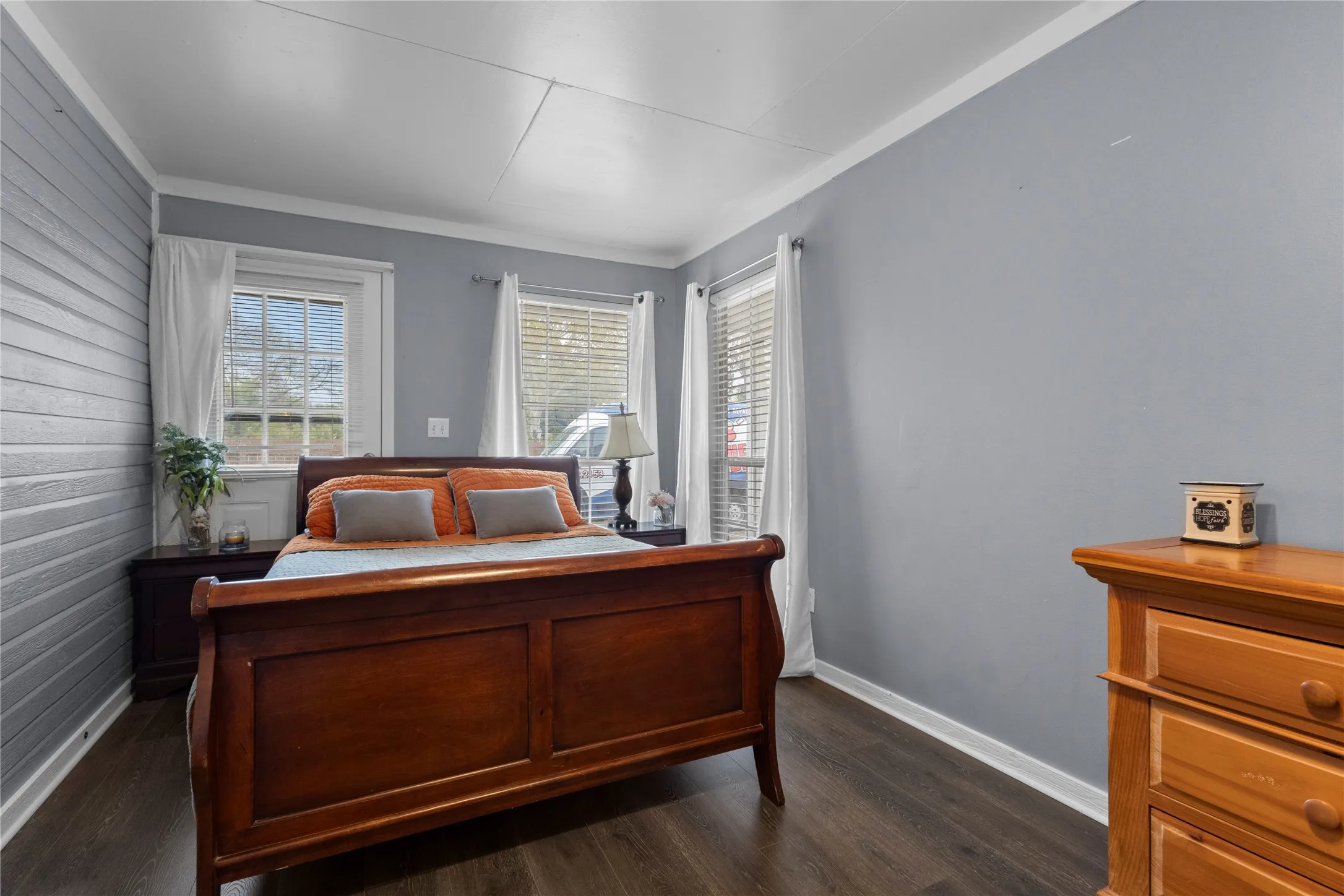 Wood-finish flooring, accent shiplap wall, multiple windows, crown molding, and painted walls