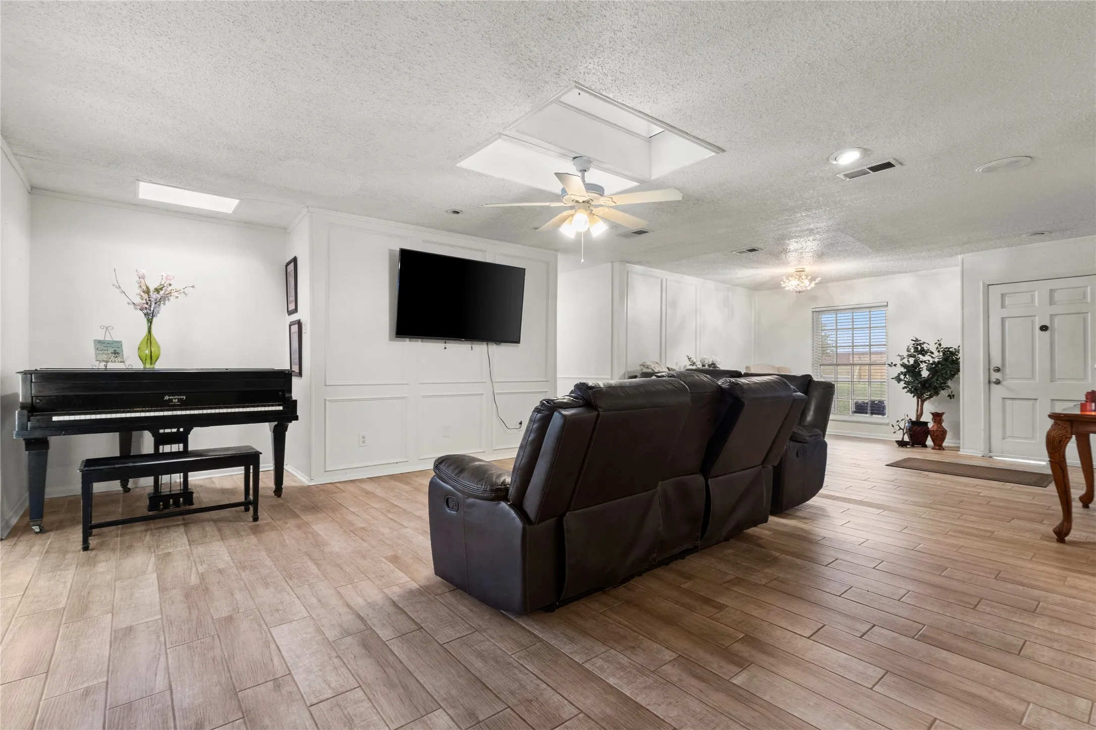 Spacious living area featuring wood-finish flooring, white paneled accent walls, recessed lighting, and a ceiling fan
