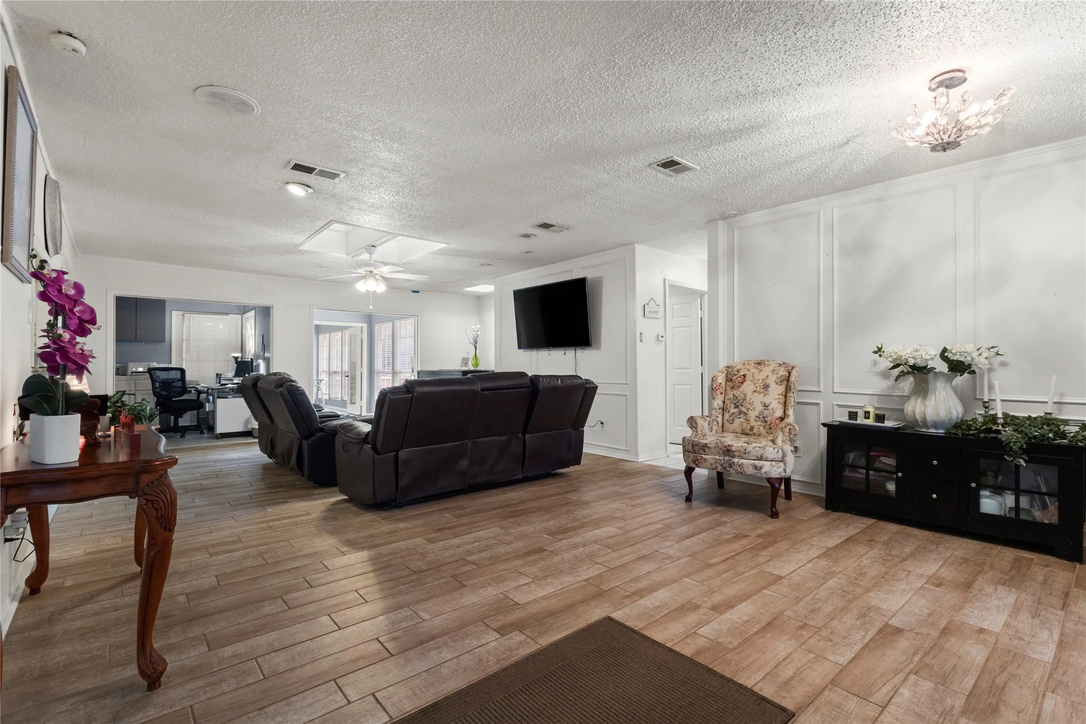Wood-finish flooring throughout, white paneled accent wall, recessed lighting, and a crystal chandelier