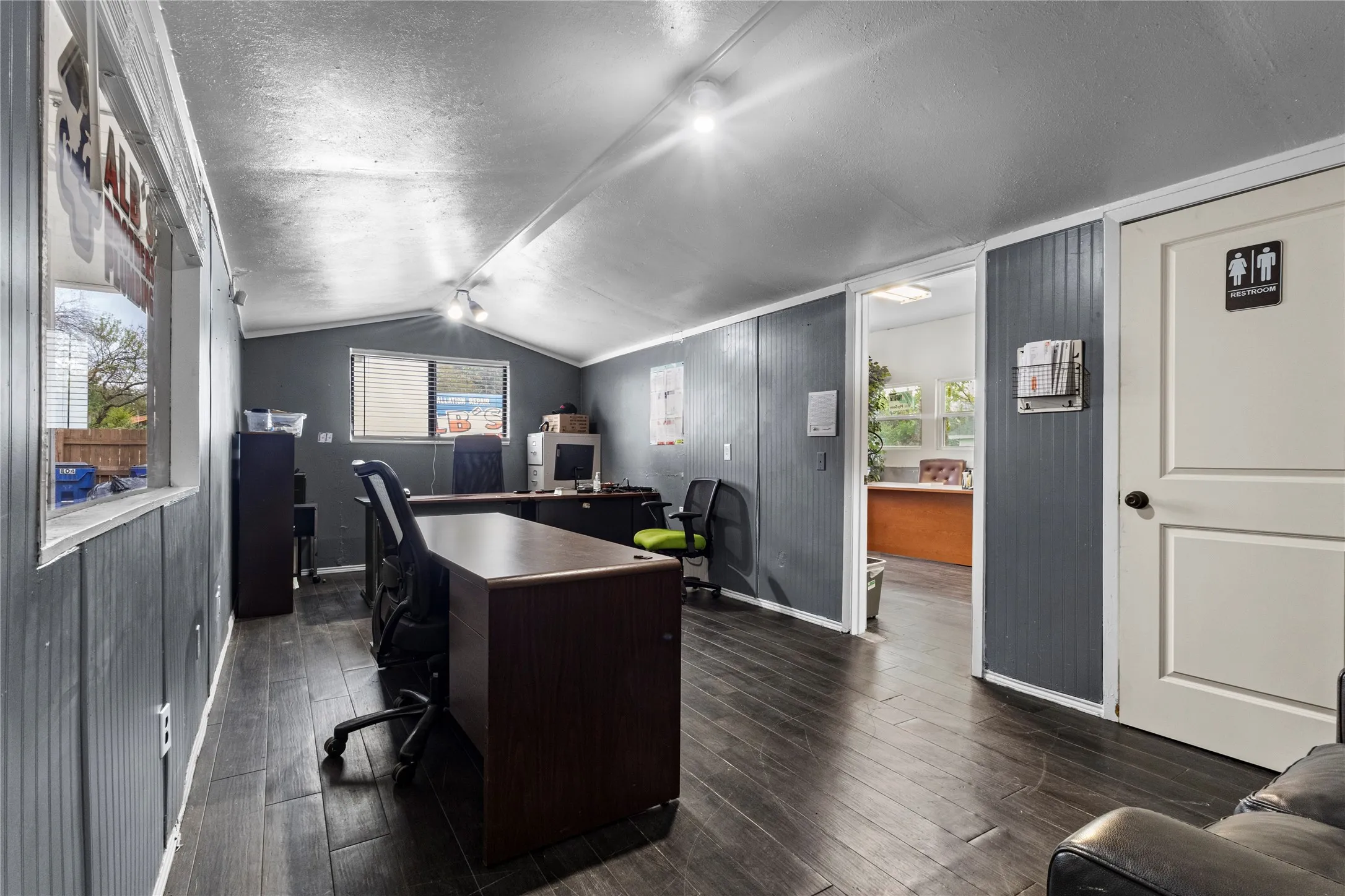 Vaulted ceiling, wood-finish flooring, paneled wall finishes, track lighting, and a white interior door