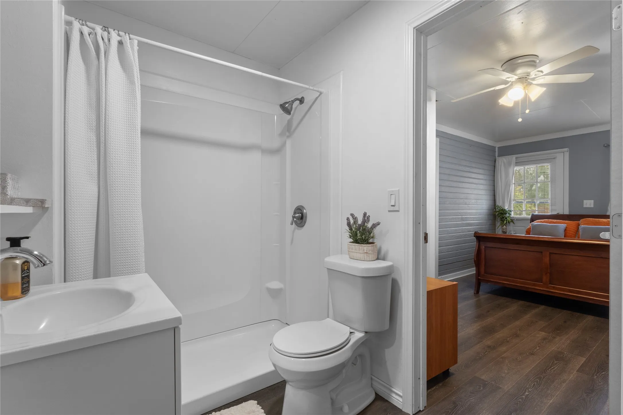 White vanity with an integrated sink, shower-tub combination, and wood-finish flooring