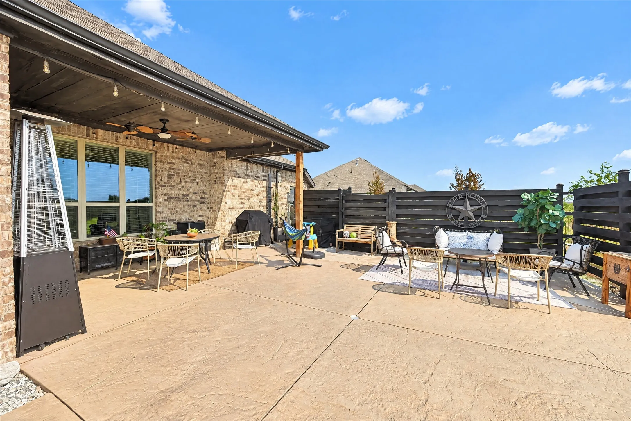Expansive stamped concrete patio with an attached covered porch featuring a ceiling fan, string lights, and brick exterior