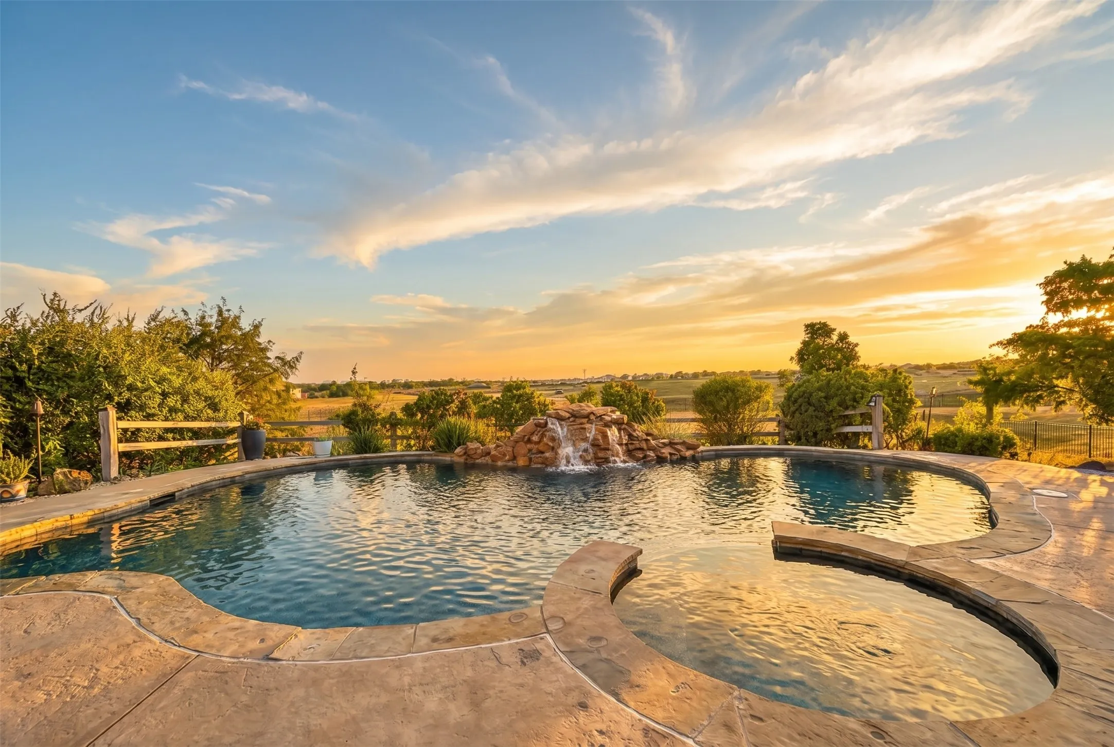 Curved swimming pool with an integrated spa, rock waterfall feature, and surrounding concrete decking