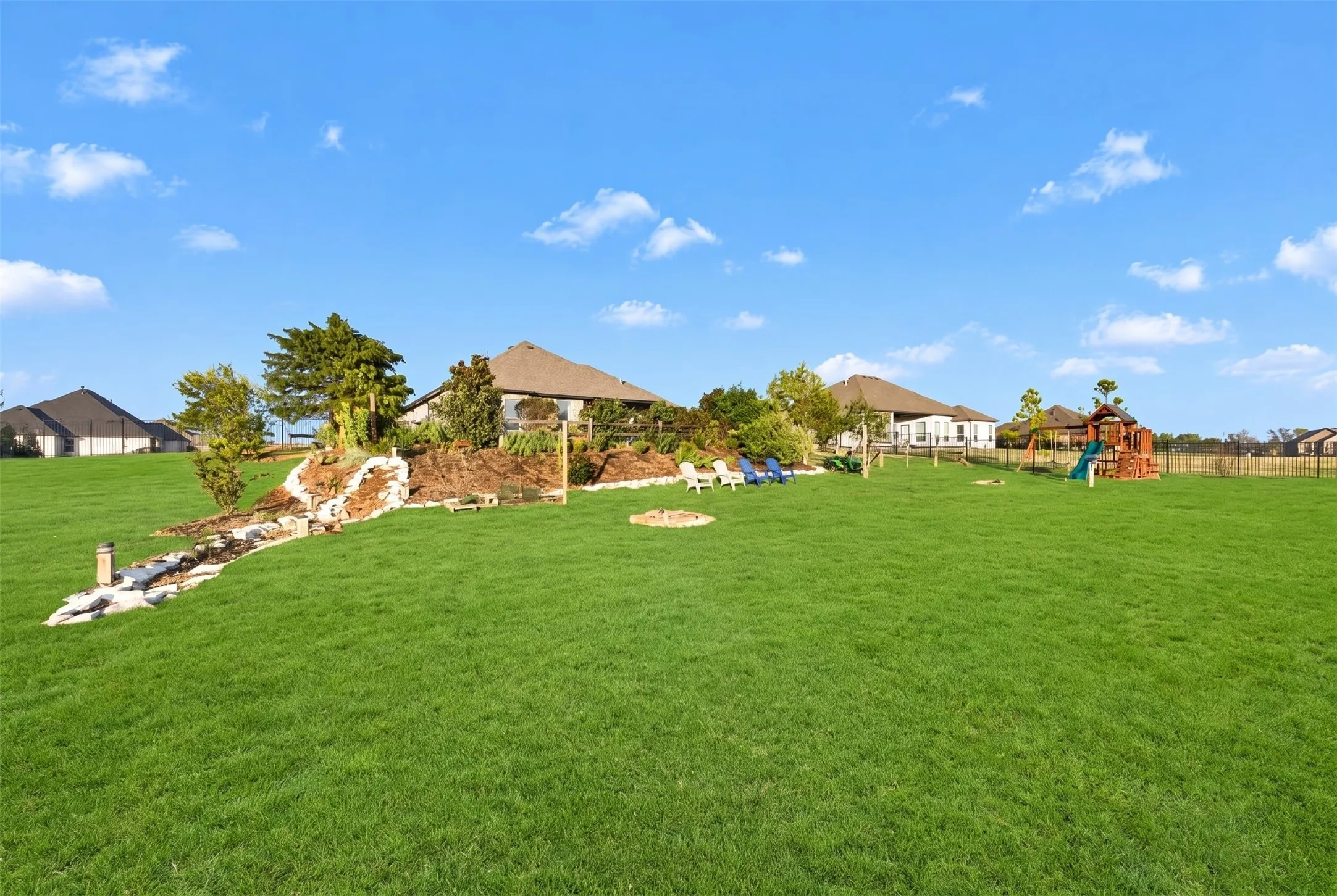 Expansive green lawn with a landscaped mound, fire pit, and partial fencing