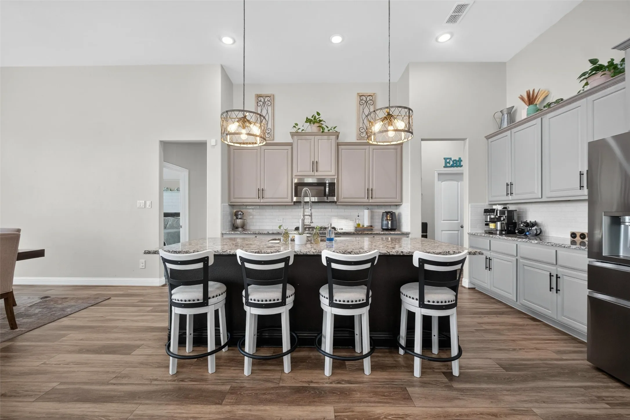 Kitchen featuring wood-finish flooring, an island with a granite countertop, light-toned cabinetry with dark hardware, a subway tile backsplash, and recessed lighting