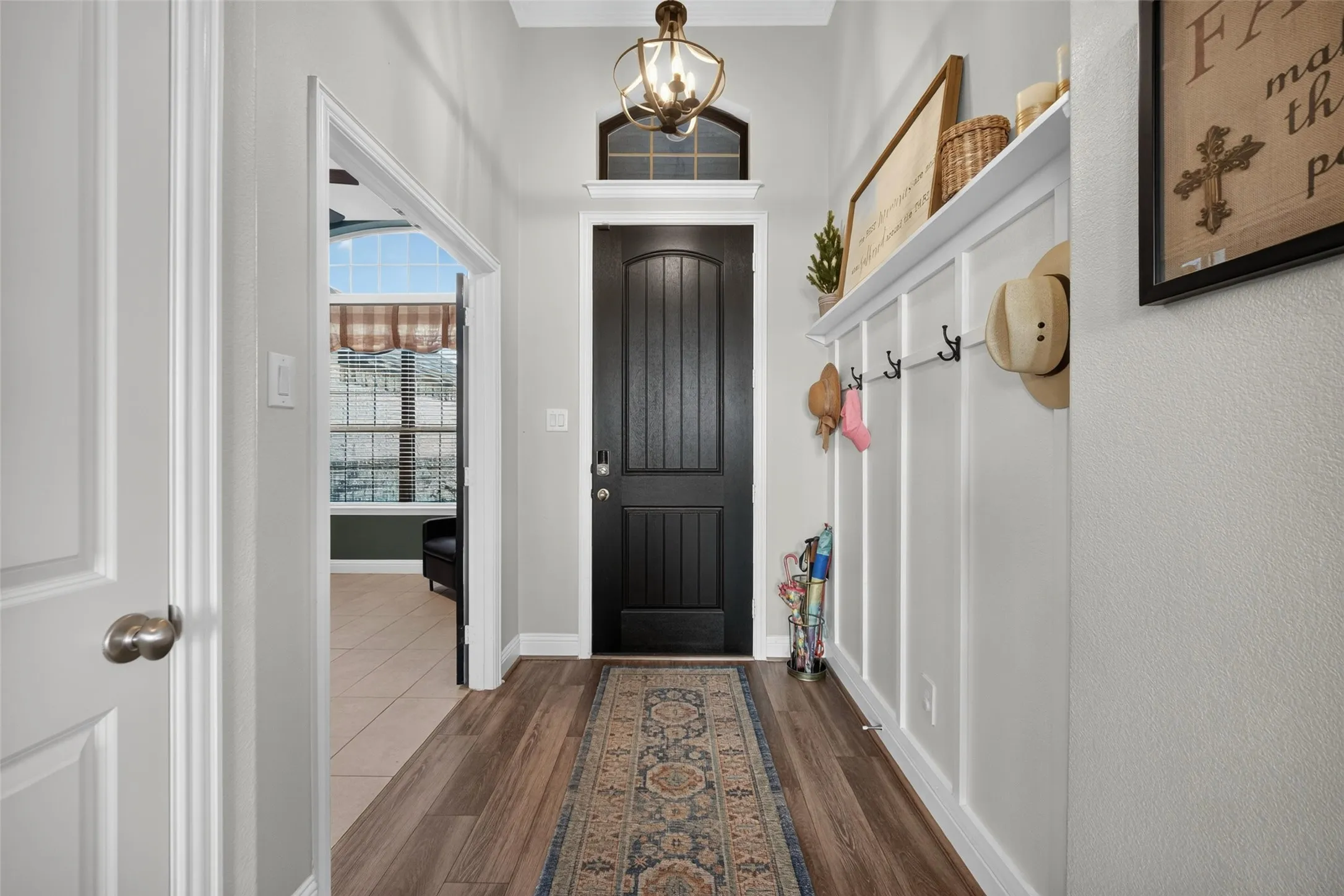 Entryway featuring wood-finish flooring, a dark paneled door with an arched transom, a built-in board and batten wall with a shelf and hooks, and a decorative pendant light fixture