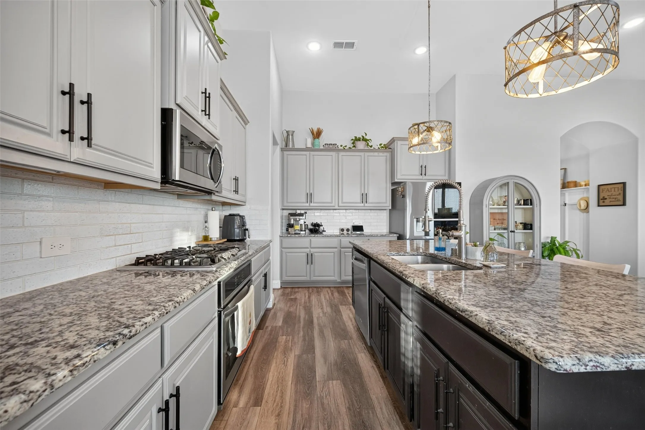 Kitchen featuring granite countertops, a gas cooktop with an oven, light-toned upper cabinetry, and a central island with dark lower cabinetry