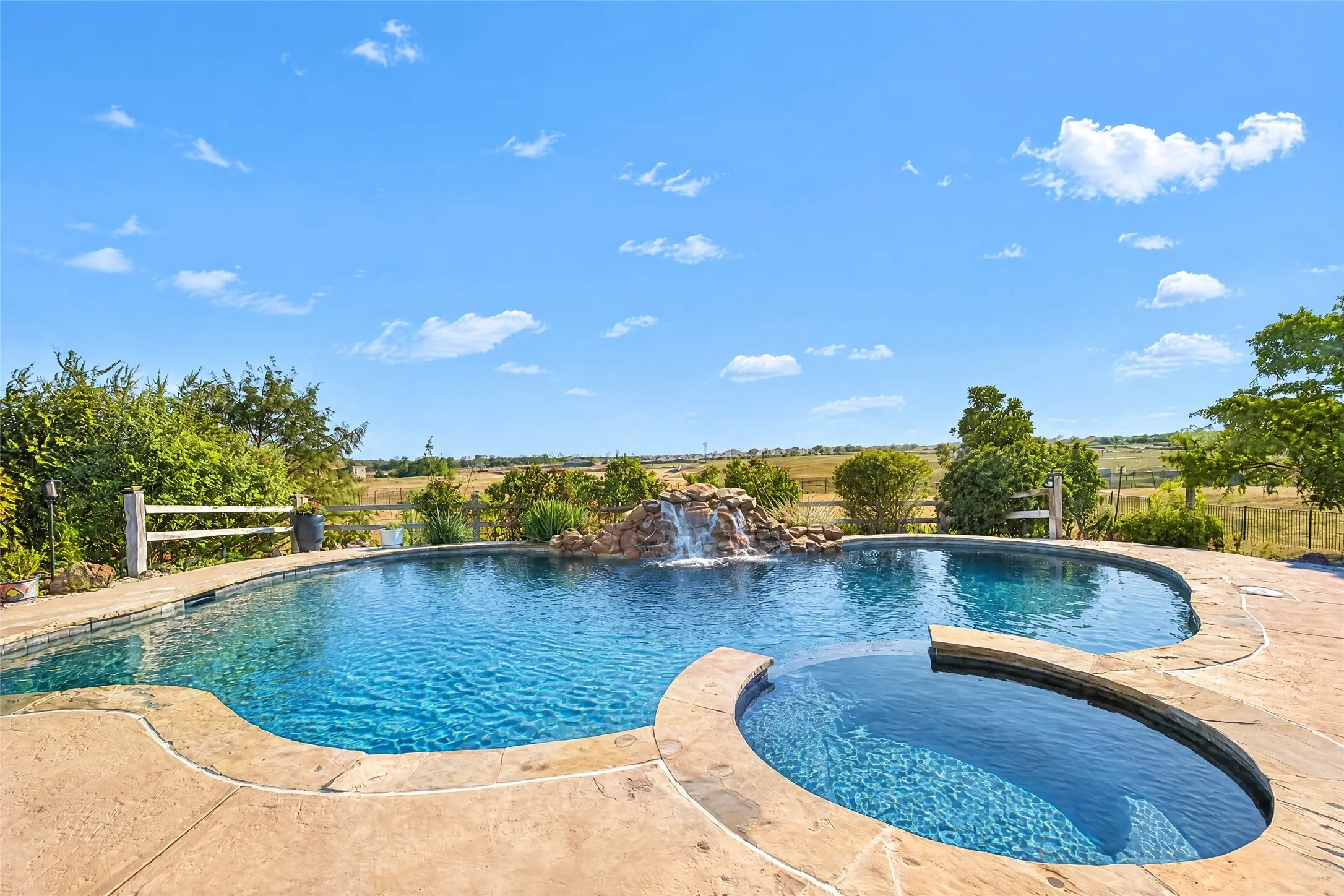 Freeform swimming pool with integrated spa and waterfall feature, surrounded by stamped concrete decking