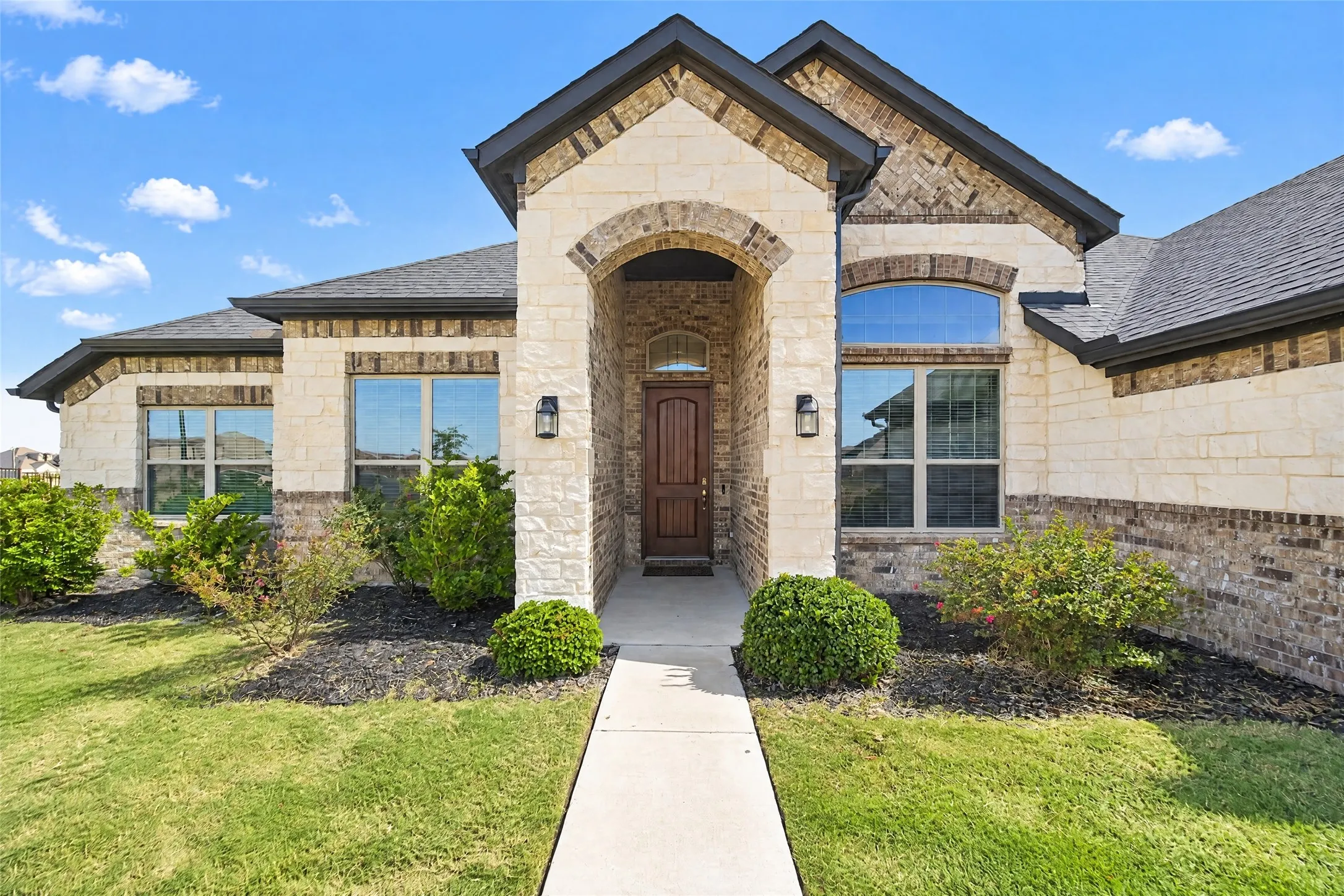 Stone and brick exterior with dark shingle roofing, arched entryway, and dark wood-paneled door