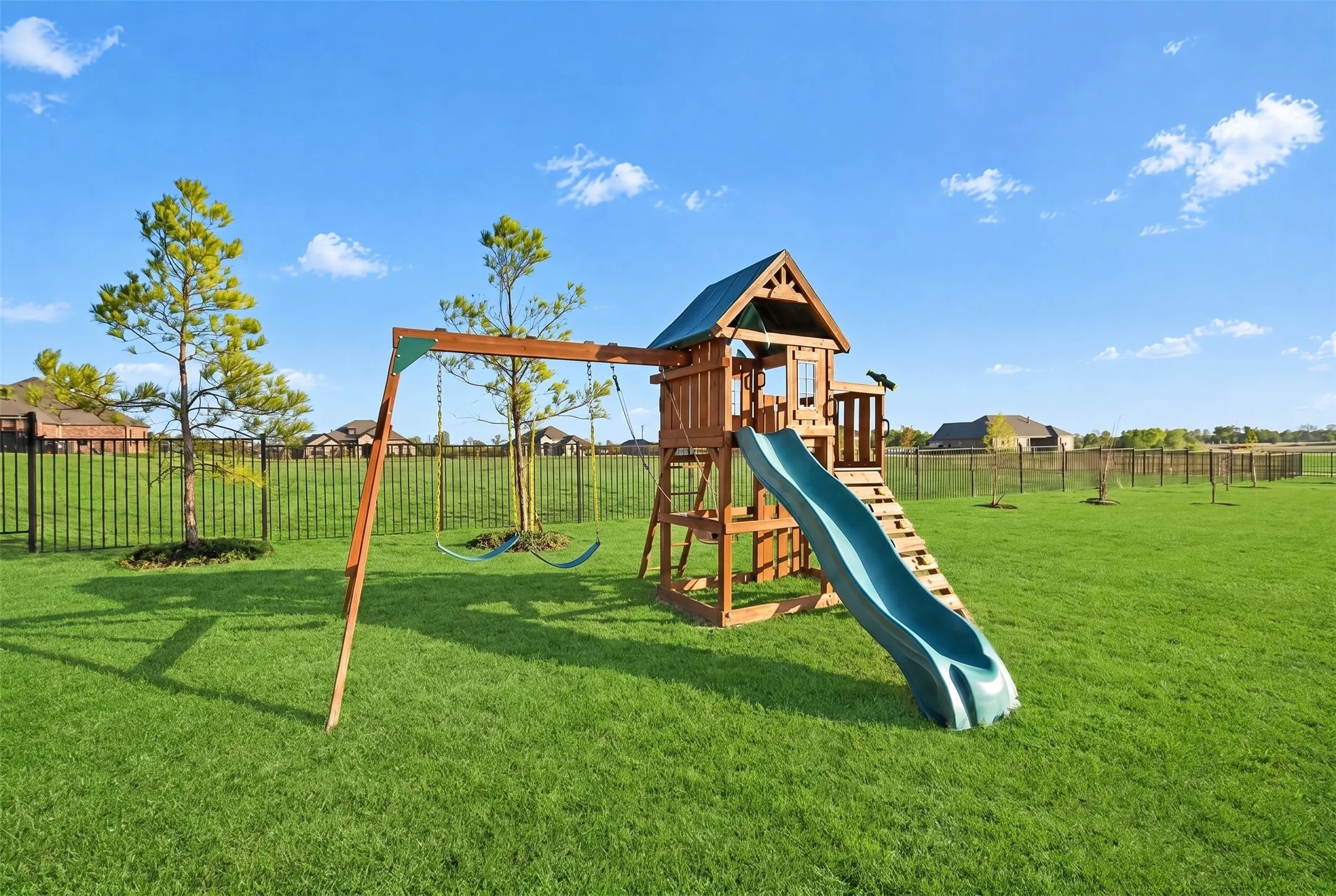 Expansive green space featuring a wood-structure playset with a slide and swing set, and mature landscaping