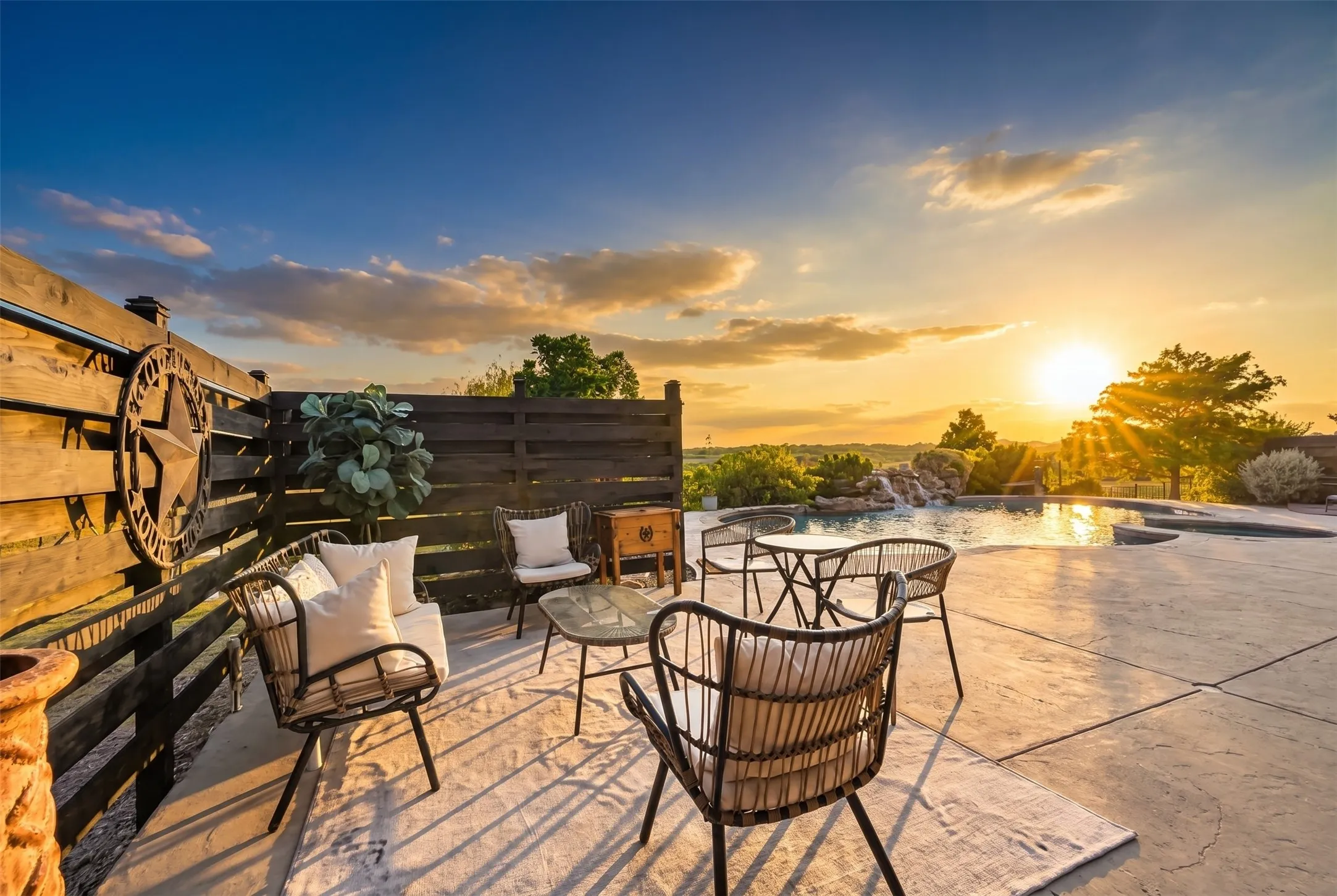 Expansive stamped concrete patio with an integrated swimming pool, featuring a waterfall element and a surrounding wood fence