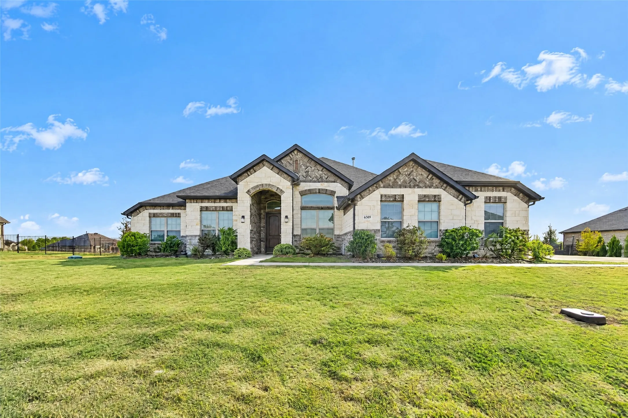 Stone and stucco exterior with an arched entryway, gabled roof, and landscaping