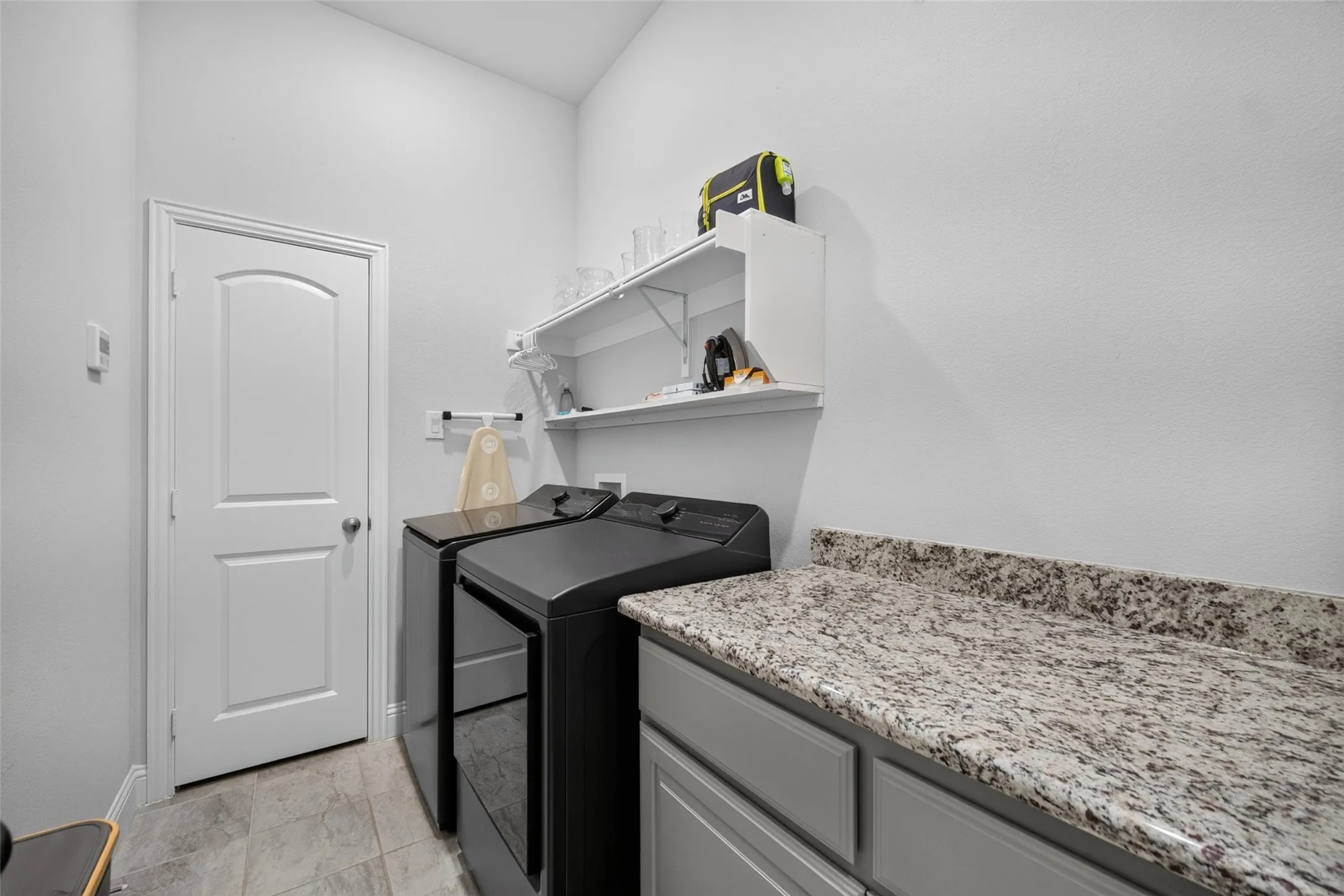 Utility area featuring a granite-style countertop, gray cabinetry, tile flooring, and wall-mounted shelving