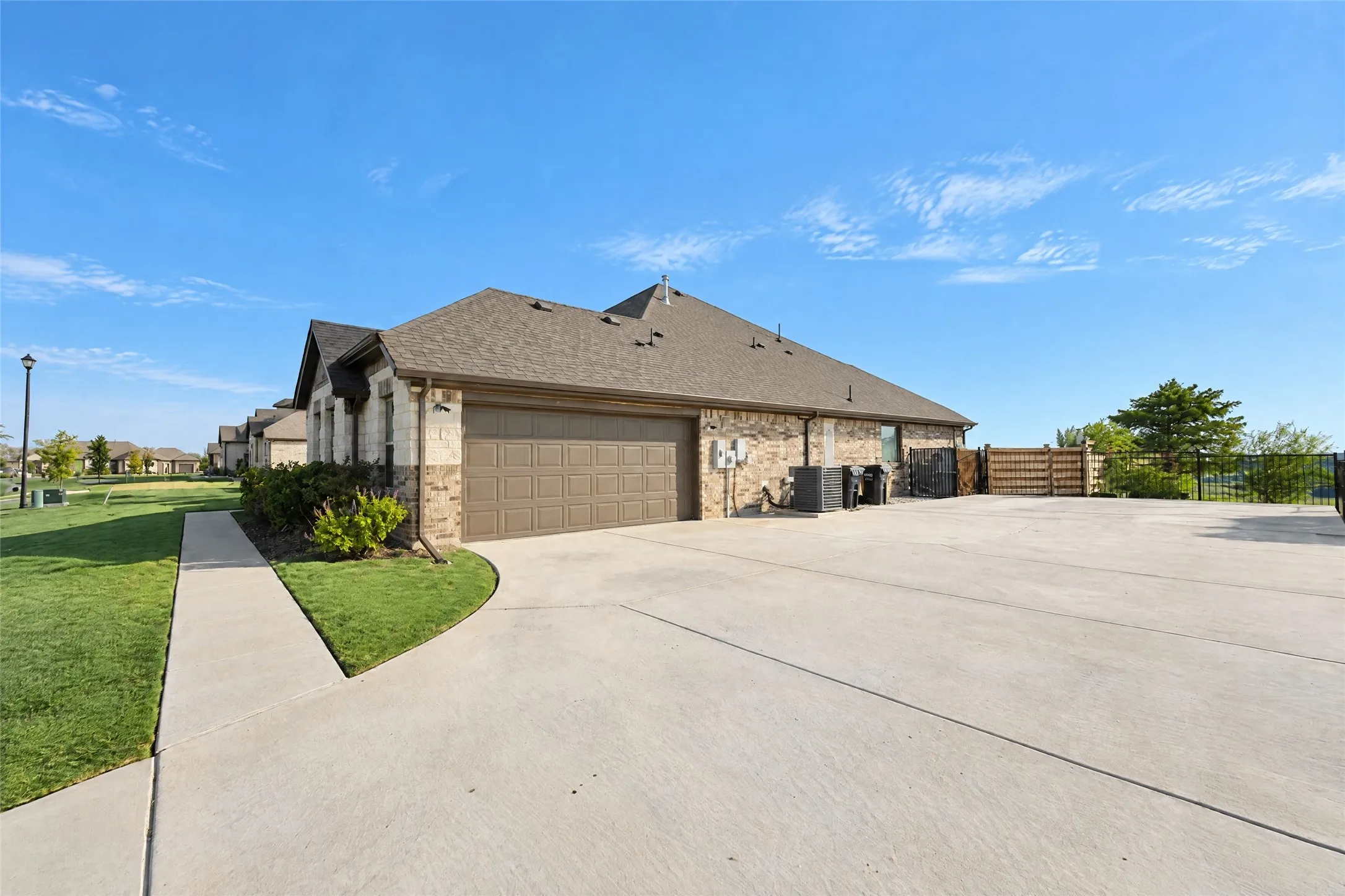 Brick and stone exterior with an attached garage, concrete driveway, and a gated side yard