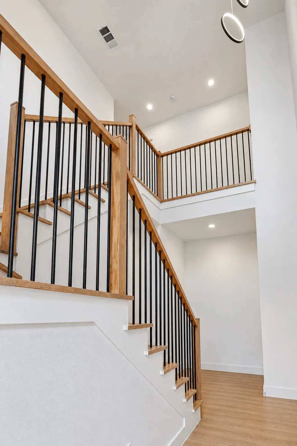 Two-story entryway featuring wood-finish flooring, a staircase with wood-finish handrails, and black metal balusters
