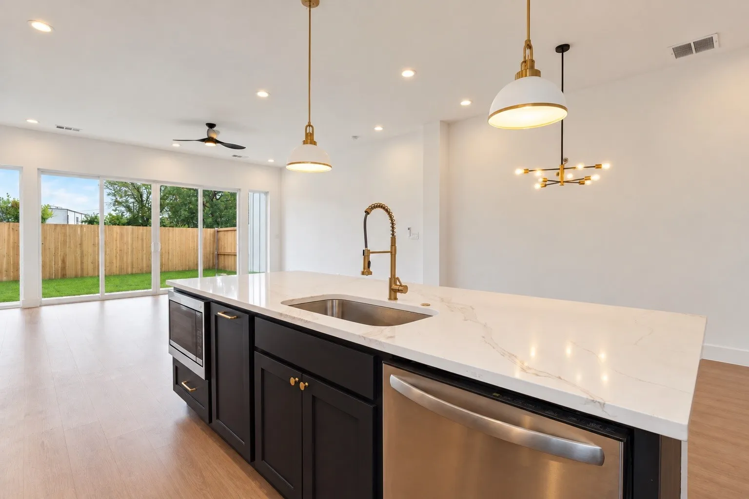 Kitchen island with a white countertop and integrated sink, stainless steel dishwasher, wood-finish flooring, and pendant lighting