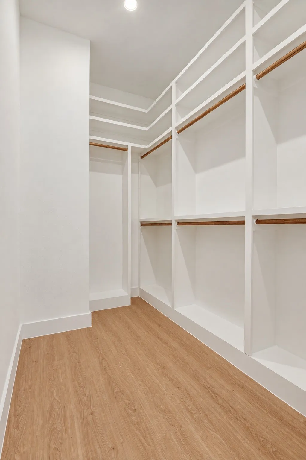 Walk-in closet featuring extensive built-in shelving, multiple hanging rods, recessed ceiling lighting, and wood-finish flooring
