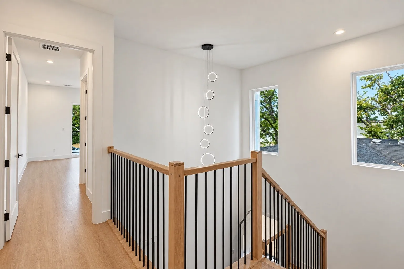 Contemporary pendant lighting, wood-finish flooring, staircase with natural wood railing, black metal balusters, and recessed ceiling lights