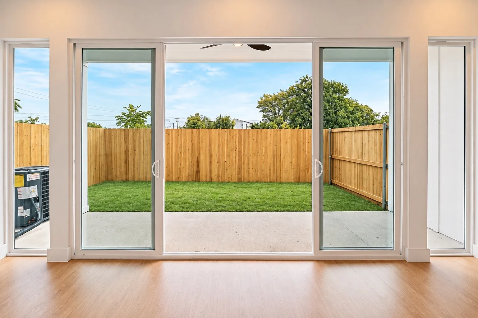 Expansive sliding glass doors opening to a private backyard with a manicured lawn, concrete patio, and wood privacy fencing