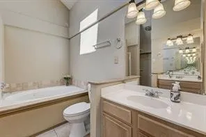 Bathroom featuring a jetted tub, ceramic tile surround, a built-in vanity with dual sinks, and a large mirror