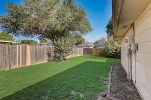 Expansive backyard featuring a manicured lawn, established shade tree, wood privacy fencing, and a neutral-toned siding exterior