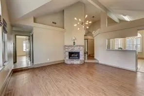 Vaulted ceilings with exposed beams, wood-finish flooring, and a stone-clad fireplace with a hearth