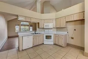 Kitchen featuring L-shaped cabinetry, white appliances, and tiled flooring