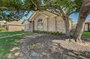Brick-clad exterior with arched window, established tree, manicured lawn, and landscaped beds