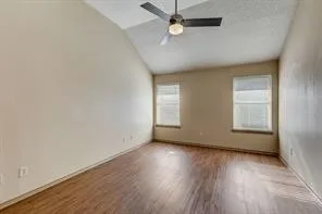 Vaulted ceiling, wood-finish flooring, ceiling fan with integrated lighting, and two windows with blinds