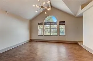 Vaulted ceiling with an architectural chandelier, arched window, wood-finish flooring, and recessed lighting