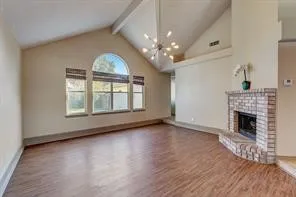 Vaulted ceilings with exposed beams, wood-finish flooring, a brick fireplace, and a large arched window