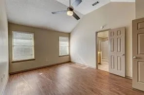 Vaulted ceiling with a ceiling fan, wood-finish flooring, two windows with blinds, and paneled doors