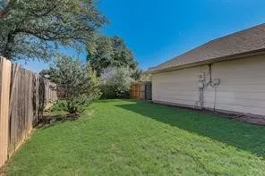 Expansive fenced yard featuring a manicured lawn, mature trees, and a durable wood fence