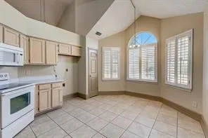 Tile flooring, vaulted ceiling, arched window, plantation shutters, and wood-finish cabinetry