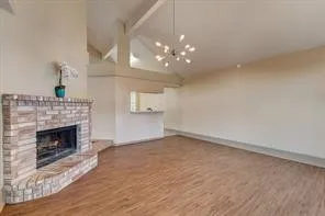 Vaulted ceiling with exposed beams, brick fireplace, wood-finish flooring, and a modern chandelier