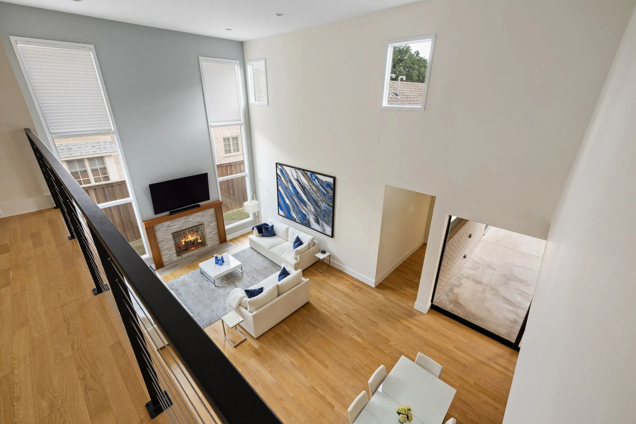 Two-story living area with wood-finish flooring, a stone-clad fireplace, and multiple tall windows